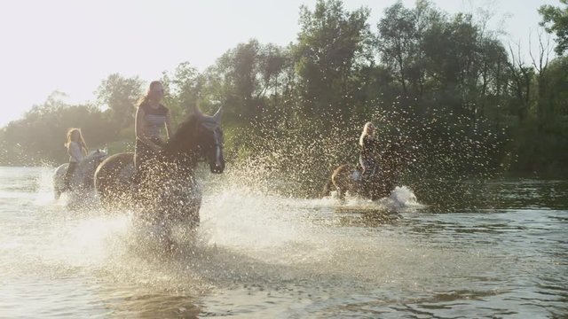 CLOSE UP: Horses splashing water around and playing in river with riders