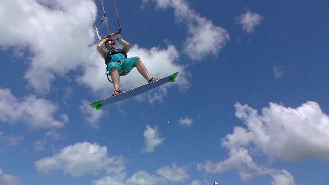 SLOW MOTION: Kite surfer has fun jumping over camera, splashing water drops
