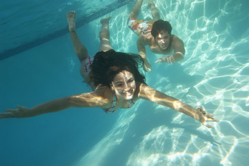 A happy young couple swimming underwater in pool - Powered by Adobe