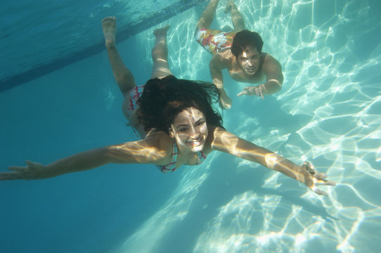 A happy young couple swimming underwater in pool