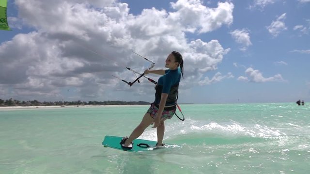 SLOW MOTION: Happy surfer girl kiteboarding past the camera in beautiful lagoon