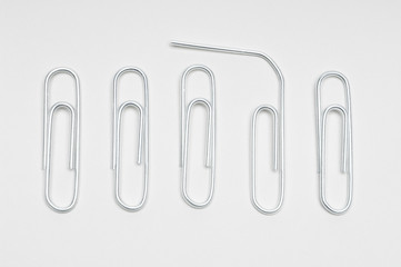 Row of steel paperclips with broken clip over white background