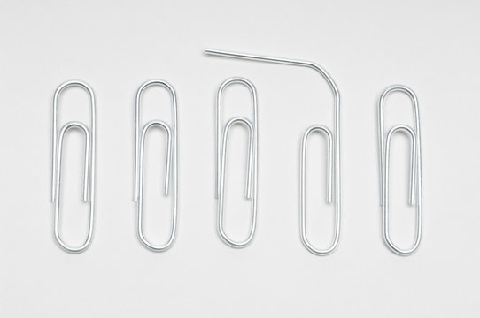 Row of steel paperclips with broken clip over white background