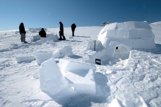 Inuit cutting snow blocks using a saw and a knife to make an igloo, Nunavut, Canada