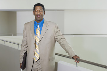 Portrait of a happy African American businessman standing by balustrade in office building