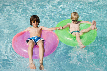 Friends enjoying on float tubes in swimming pool - Powered by Adobe