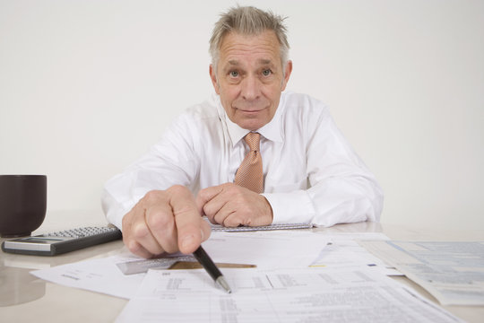 Portrait of a confident senior businessman with paperwork at desk - Powered by Adobe