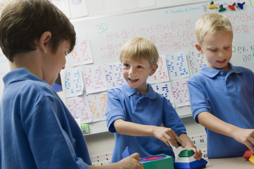 Three happy preadolescent boys solving puzzle game in a playschool