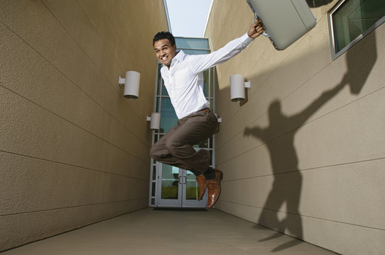 Happy young successful businessman jumping against entrance of office building