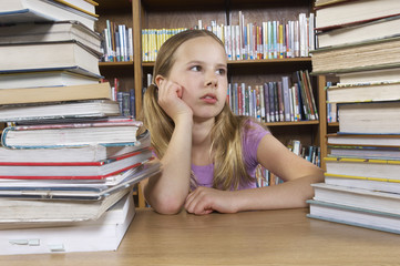 Young girl looking at stack of books on desk in library