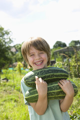 Portrait of happy young boy holding marrows in community garden