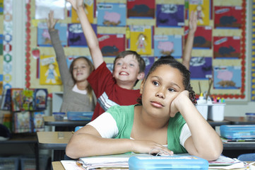 Young girl getting bored while classmates raising hands in background