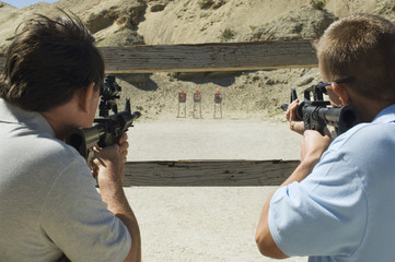 Rear view of two men aiming rifles at firing range during combat training
