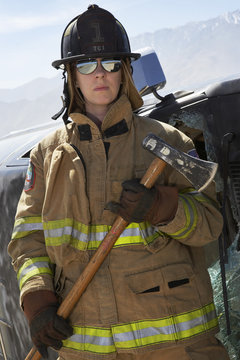 Portrait of a female firefighter holding axe by crashed car