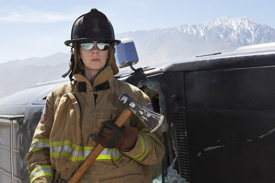 Female firefighter holding axe by a crashed car