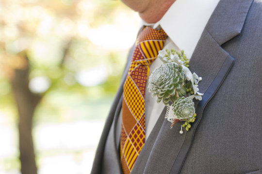 Groom with a Seedum Succulent Chicks and Hens Boutonniere on a Gray Suit with a Yellow and Orange Patterned Tie