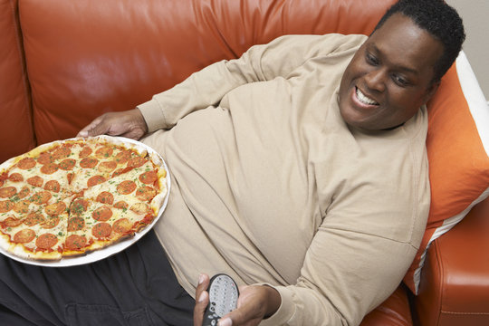 High angle view of an obese African American man watching television with pizza on lap