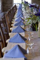 Very Long Wedding Reception Table with White Tablecloth and Wooden Chairs; Purple Napkins and Centerpieces