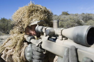 US army soldier in grass camouflage pointing rifle