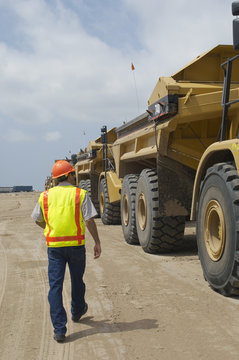 Rear view of a worker walking near trucks at landfill site