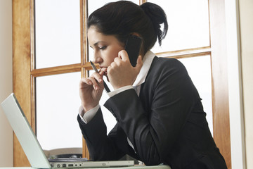 Young businesswoman on call using laptop in office
