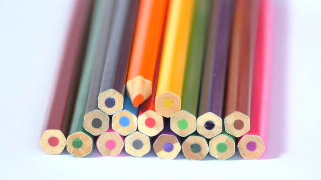 Pencils of different colors are set in shape of pyramid and one orange pencil is turned in oposite direction, then all wooden pencils are laid down in one line. Close up, 4K Ultra HD.