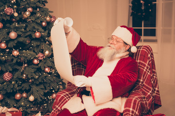 Aged happy Santa Claus reading wishes of xmas presents