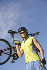 Naklejka premium Low angle view of a happy young man carrying bicycle against sky