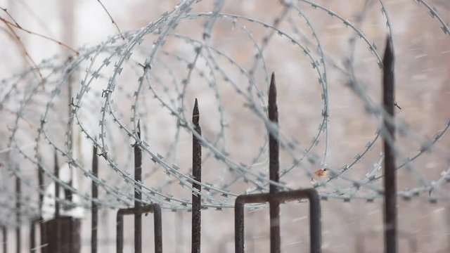 Barbed wire on metal fence with pointed rods. Snowflakes fall slow.