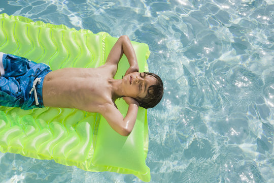 Boy floating on inflatable mattress in swimming pool
