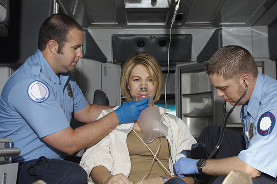 Male paramedics giving oxygen while taking pulse of victim in ambulance