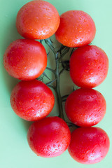  red tomatoes with green leaves. Top view. Green background.