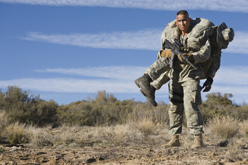US Army soldier carrying wounded friend on shoulder during a mission