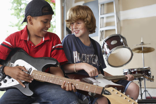 Happy multiethnic boys playing guitars in garage