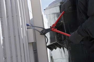 Closeup of a thief's hands cutting wire with cutter to open the gate