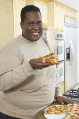 Portrait of an obese African American man holding slice of pizza at kitchen counter