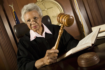Senior female judge holding gavel and law book in courtroom
