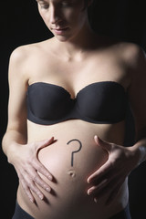 Young pregnant woman with question mark on abdomen isolated over black background