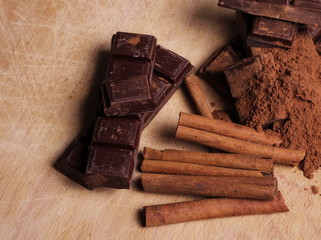 chocolate bars with cinnamon sticks and pile cocoa powder on wooden chopping board