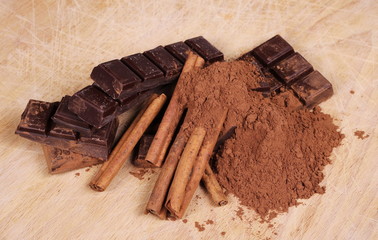 chocolate bars with cinnamon sticks and pile cocoa powder on wooden chopping board