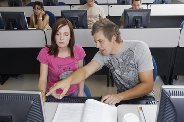 Male student pointing towards computer screen with classmates in the background