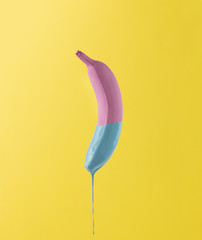 Pink banana with dripping blue paint on yellow background. Minim