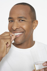 Portrait of an African American man taking pill as he holds glass of water