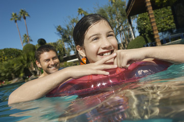 Happy preadolescent girl with father enjoying in swimming pool at resort