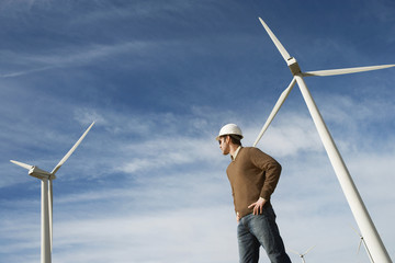 Low angle view of a male engineer standing against turbine at wind farm