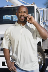 Portrait of an African American truck driver using cell phone in front of a truck