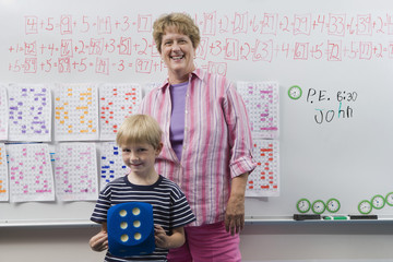 Portrait of a happy female teacher standing with little boy in front of class