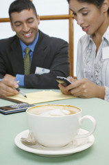 Closeup of a cappuccino cup with business people working in the background