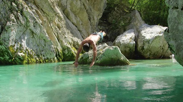 CLOSE UP: Cheerful man jumping head first into crystal clear water and swimming