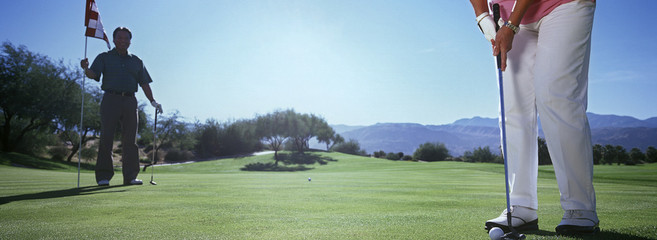 Low section of a woman playing golf with man holding flag on ground